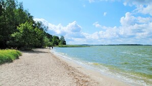 A sandy beach with a calm water body, surrounded by dense greenery and trees.