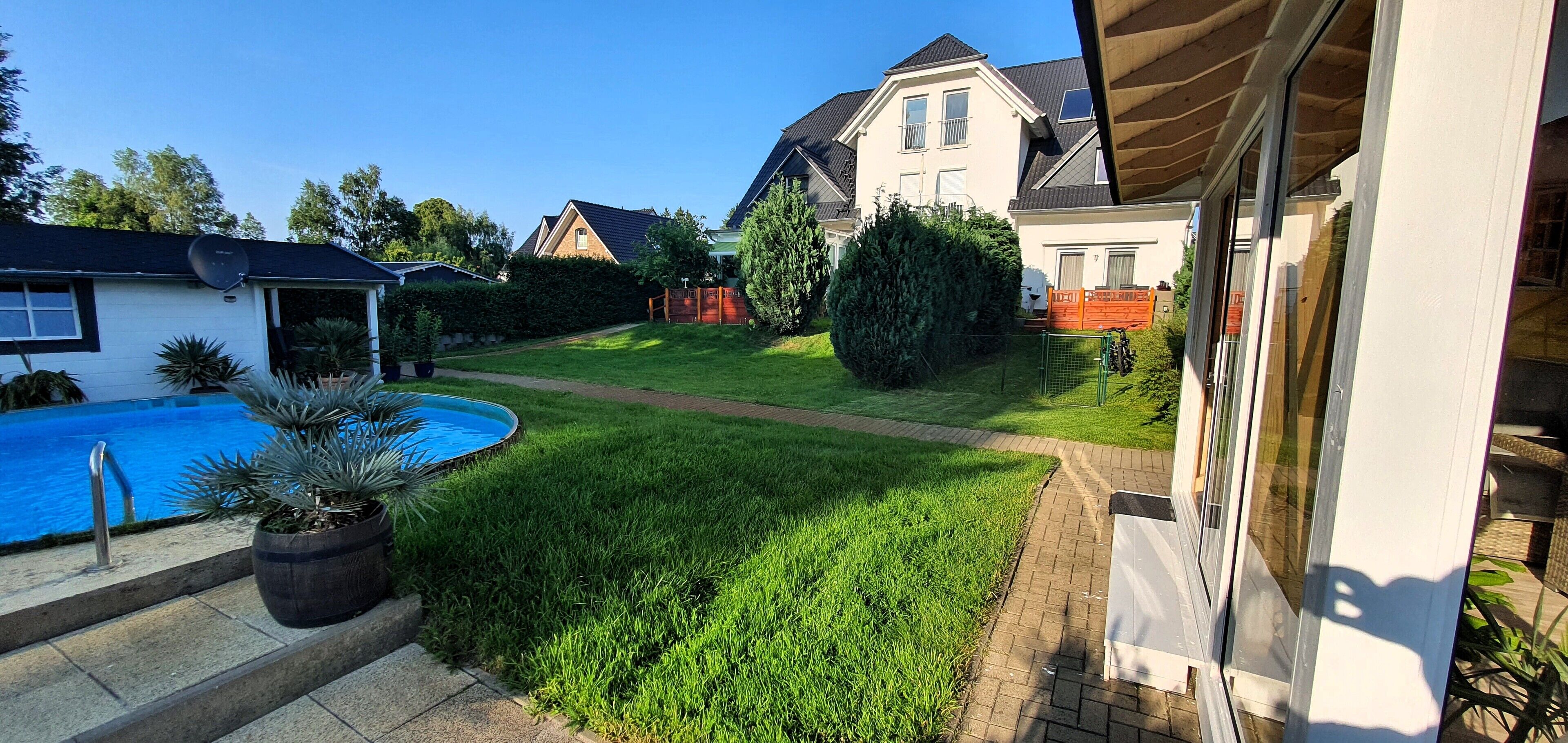 A residential backyard with a swimming pool, a well-maintained lawn, and a large house with a sloped roof.