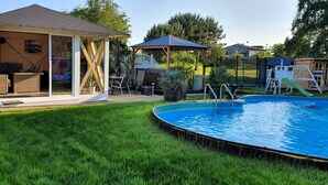 A backyard with a swimming pool, a covered seating area, and a children's play structure.