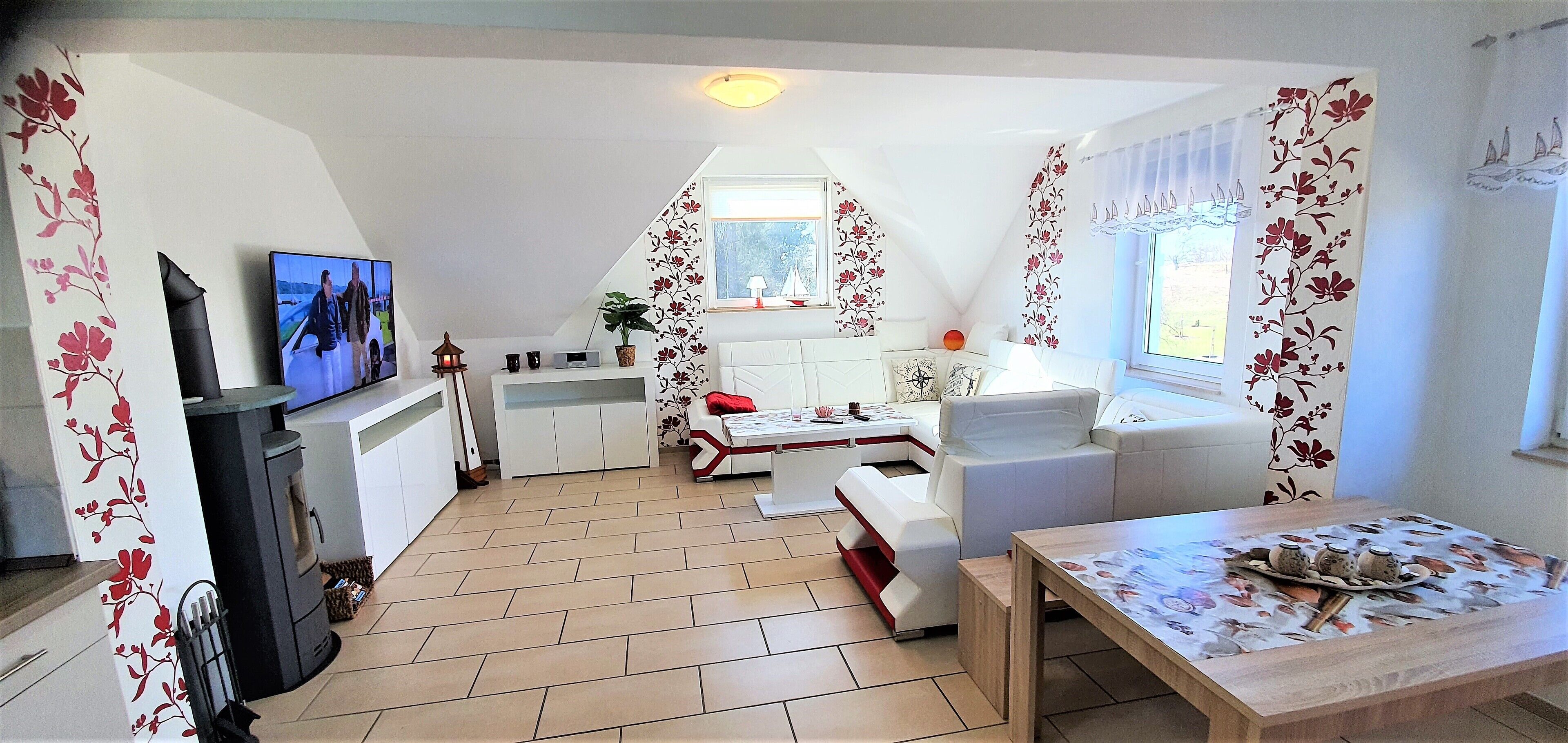 A modern kitchen with a TV, a dining area with a table set for two, and a cozy seating area with a sofa and armchairs.