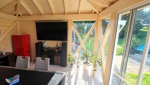 A cozy wooden cabin with a TV, seating area, and large windows overlooking a garden.