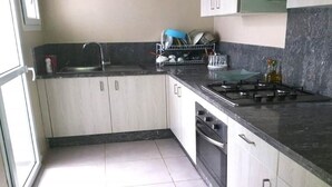 A kitchen with white cabinets, a black countertop, a stove, and a dish rack with utensils. - Beautiful apartment in Fal Azur 4388 (Bouznika)