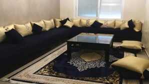 A living room with a dark blue sofa, gold and black cushions, a glass coffee table, and a patterned rug. - Beautiful apartment in Fal Azur 4388 (Bouznika)