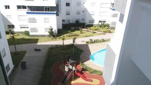 A playground with slides and a small pool, surrounded by a landscaped area with trees and a building in the background. - Beautiful apartment in Fal Azur 4388 (Bouznika)