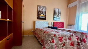 Une chambre à coucher comprenant un lit, une armoire, deux tableaux, une lampe suspendue et une fenêtre avec des rideaux.