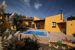 Una villa amarilla con piscina, mobiliario de exterior y jardín.