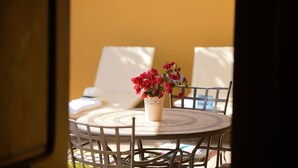 A round table with a white lace tablecloth, surrounded by white chairs, and a vase with red flowers in the center.