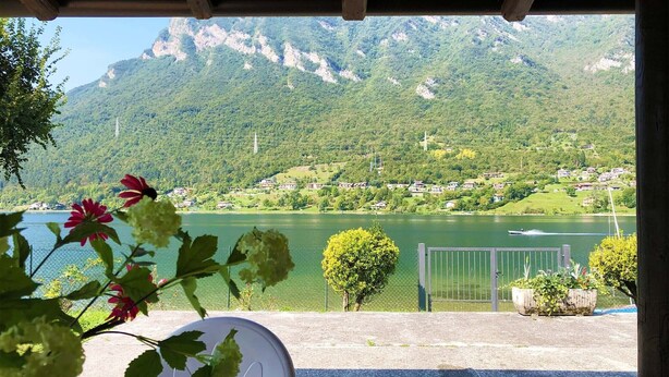 A view of a lake with mountains in the background, a chair, and a potted plant in the foreground.