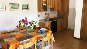 A kitchen with wooden cabinets, a dining table with a floral tablecloth, and a vase with flowers. - Directly on the lake (Crone)