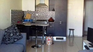 A compact kitchen with a gas stove, a microwave, and a sink. There is a bar stool and a small trash bin. - Residence Islane Agadir 4282 (Agadir)
