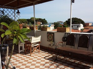 A balcony with a checkered floor, a wooden chair, a metal bench, and potted plants.