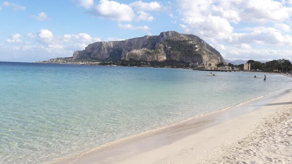 A beach with clear water, a sandy shore, and a large rock formation in the background.