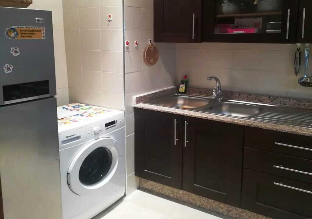 Una cocina compacta con lavadora, pileta, alacenas oscuras y un salpicadero de azulejos.
