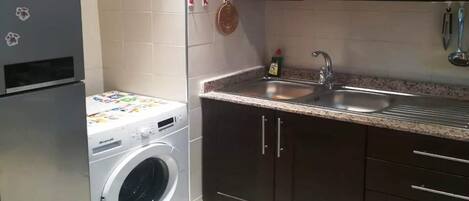 Una cocina compacta con lavadora, pileta, alacenas oscuras y un salpicadero de azulejos.