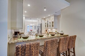A kitchen with a central island, bar stools, and a view into the dining area.