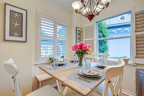 A dining area with a table set for four, a chandelier, and a window with blinds. - Siesta Bayside Villa: Water Views & Private Beach (Siesta Key)