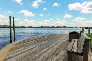 A wooden deck with a bench and a table, overlooking a body of water with a distant shoreline. - Siesta Bayside Villa: Water Views & Private Beach (Siesta Key)