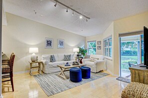 A living room with a sofa, coffee table, ottomans, and a television.