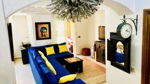 A living room with a blue sofa, a hanging light fixture, a wall clock, and a framed picture. - Beautiful apartment in Ricoflores Beach 4386 (Mohammedia)