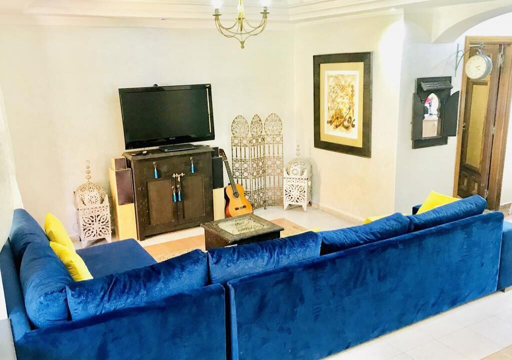 Un salón con un sofá azul, televisión, una guitarra y objetos decorativos.