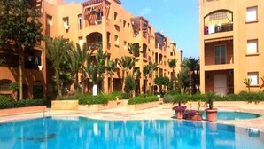 A swimming pool surrounded by palm trees and a multi-story building with balconies. - Beautiful apartment in Ricoflores Beach 4386 (Mohammedia)