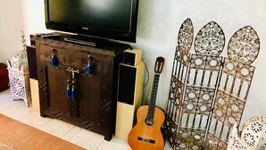A television on a wooden cabinet, a guitar, and decorative metal gates. - Beautiful apartment in Ricoflores Beach 4386 (Mohammedia)