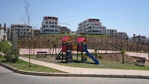 A playground with slides and climbing structures, surrounded by a paved area and benches. - Beautiful apartment in Lilacs Garden 4539 (Cabo Negro)