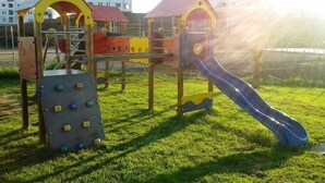 A playground with climbing structures and a slide, set on a grassy field with buildings in the background. - Beautiful apartment in Lilacs Garden 4539 (Cabo Negro)