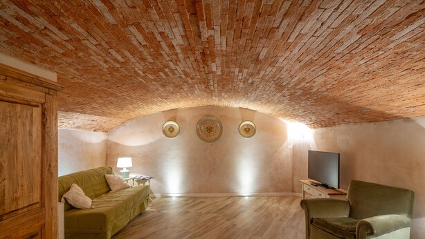 Una habitación acogedora con techo de ladrillo, un sofá verde, un sillón verde, un televisor de pantalla plana y una pequeña mesa con una lámpara.