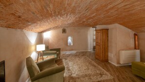 Acogedor dormitorio en ático con techo de ladrillo visto, un armario de madera, un sillón verde, una lámpara y un radiador.
