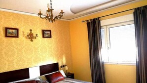 A hotel room with a bed, a chandelier, two framed pictures on the wall, and a window with curtains. - Sublime Floor Villa in Ifrane 4172 (Ifrane)
