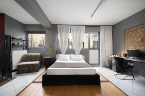 A modern bedroom with a large bed, a desk, and a chair. There is a window with curtains, a radiator, and a plant. - Zen loft in downtown-Gazi (Athina)