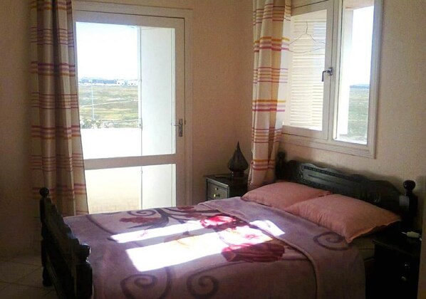 A bedroom with a bed, curtains, a window, and a nightstand.