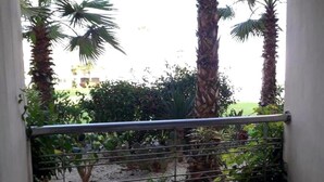 Un balcón con barandilla de metal, con vista a un jardín con diversas plantas y palmeras.
