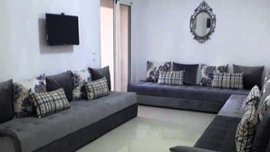 Una sala de estar con dos sofás oscuros, cojines estampados, un televisor de pantalla plana y un espejo en la pared.