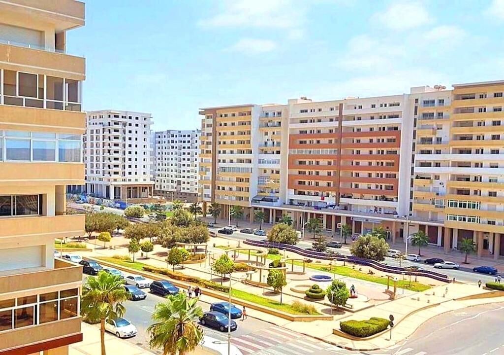 Una zona residencial urbana moderna con edificios de apartamentos de varios pisos, una rotonda central y palmeras.