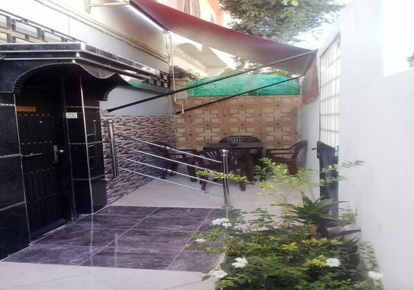 A narrow outdoor corridor with a tiled floor, a black gate, a staircase, and a small table with chairs.