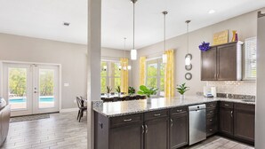 A modern kitchen with dark cabinets, granite countertops, and a built-in dishwasher. - Destin Sun | Private Pool | 6-Seater Golf Cart | 4 Mins to Beach (Destin)