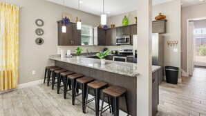 A modern kitchen with a granite countertop, dark cabinets, and bar stools. - Destin Sun | Private Pool | 6-Seater Golf Cart | 4 Mins to Beach (Destin)