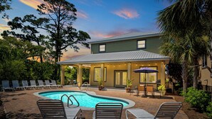 A pool area with lounge chairs, a covered patio, and a house in the background. - Destin Sun | Private Pool | 6-Seater Golf Cart | 4 Mins to Beach (Destin)