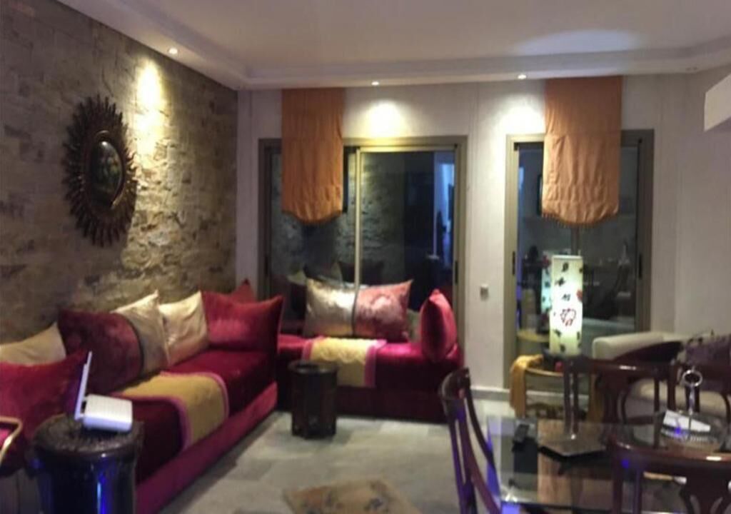 A living room with a red sofa, a coffee table, and a TV. There is a stone wall and a window with curtains.