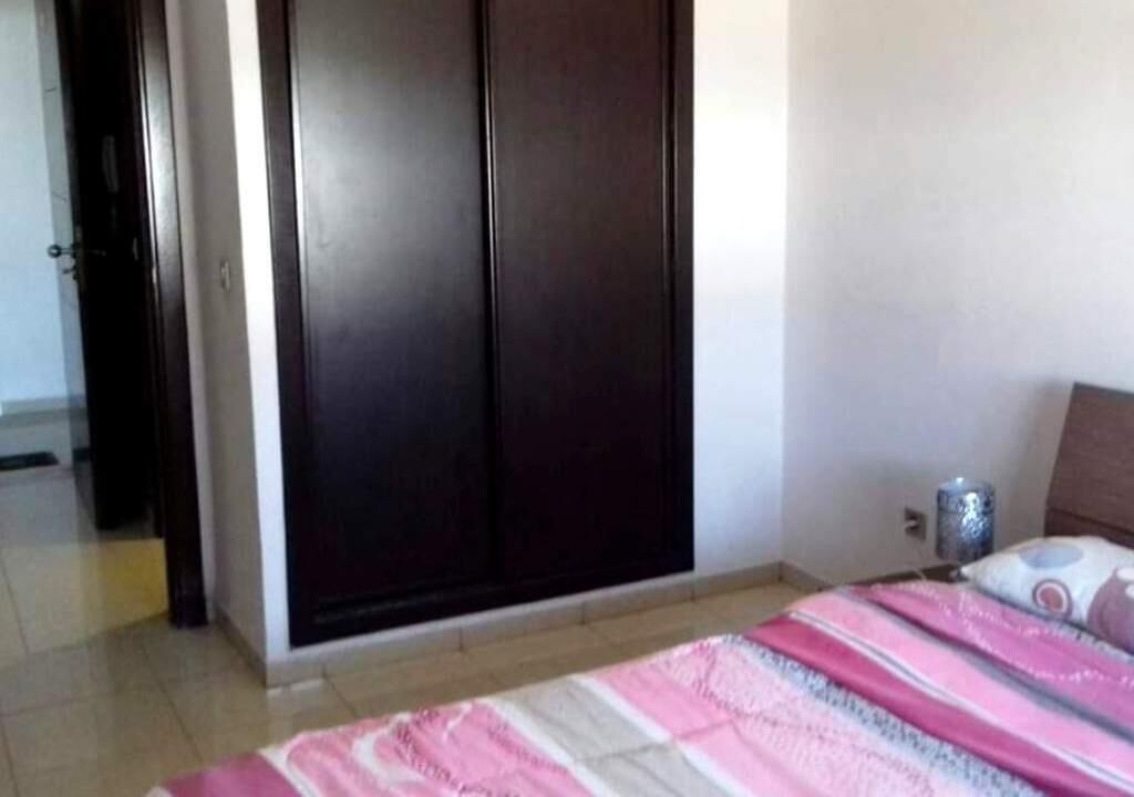 A bedroom with a bed, a dark wooden wardrobe, and a tiled floor.