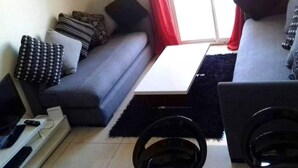 A living room with a grey sofa, black and patterned cushions, a white coffee table, and a black rug.