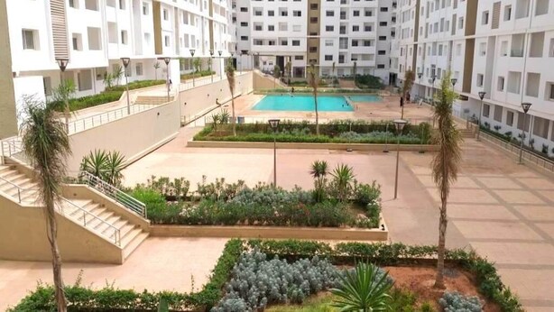 A multi-story residential building with a central courtyard featuring a swimming pool, surrounded by landscaped gardens and staircases.