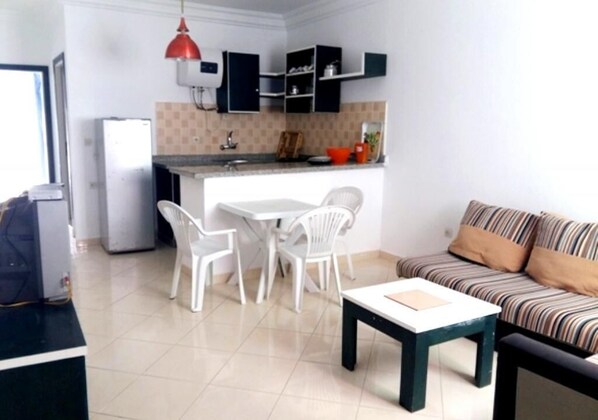 A compact living space with a kitchenette, a dining area with white chairs, a sofa with striped cushions, and a small table.