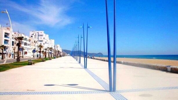 A seaside promenade with a clear sky, a beach, and buildings along the path. - Nice Studio of seaside 4376 (Martil)
