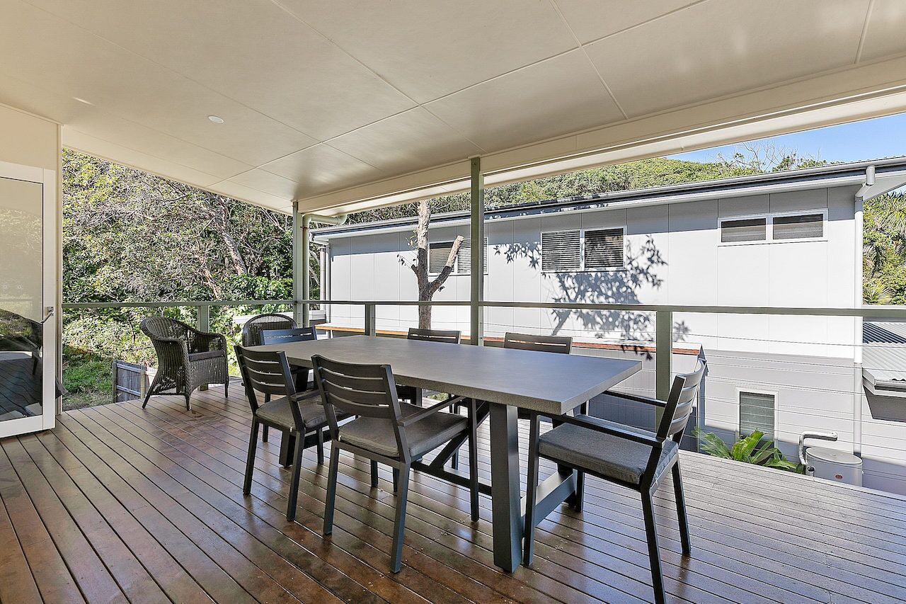 A covered outdoor patio with a dining table and chairs, a grill, and a view of a modern house.