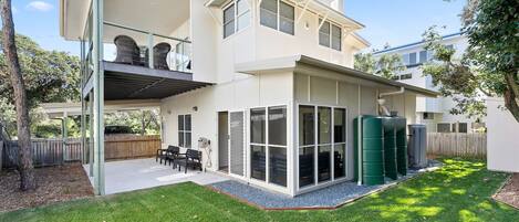 A two-story house with a covered patio, a fenced backyard, and a green water tank.