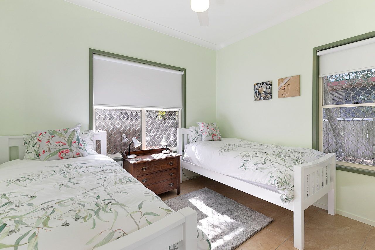 A bedroom with two single beds, a nightstand, a dresser, and a window with a view.