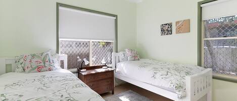 A bedroom with two single beds, a nightstand, a dresser, and a window with a view.
